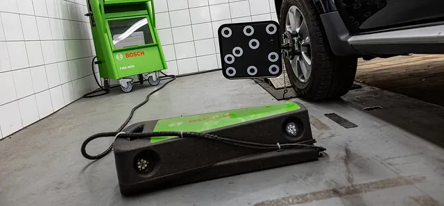 Grünes Bosch-Gerät mit Kabel auf Boden neben einem Auto in einer Werkstatt mit weiß gekachelten Wänden