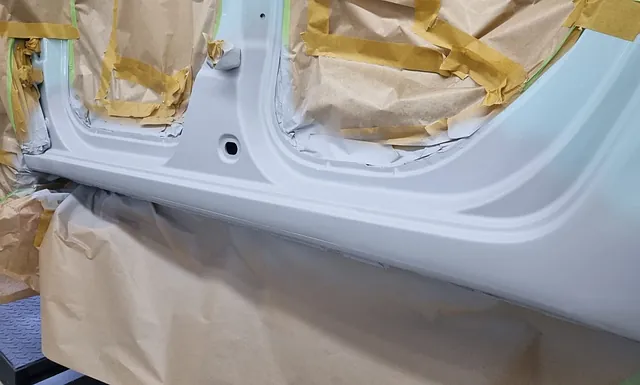 Teilansicht einer Fahrzeugtür, die mit Papier und Klebeband abgeklebt und weiß lackiert ist