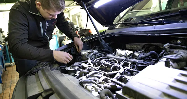 Mann arbeitet mit Werkzeug an einem geöffneten Motorraum eines Fahrzeugs in einer Werkstatt