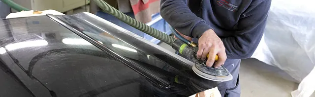 Person poliert mit einem elektrischen Poliergerät die Motorhaube eines Autos